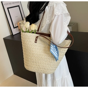 Detail of straw woven tote bag with brown leather straps and blue striped silk scarf