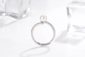Macro shot of an adjustable pearl ring with micro-paved diamonds on a white icy surface