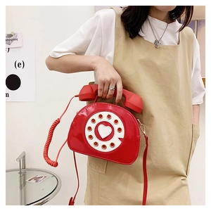 Detail of red vintage telephone-shaped crossbody bag featuring heart dial on patent leather