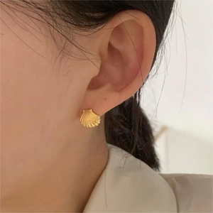 Close-up of shell-shaped gold stud earring with detailed texture on a female model