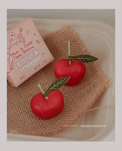 Detalle de velas aromáticas con forma de cereza roja sobre arpillera junto a una caja
