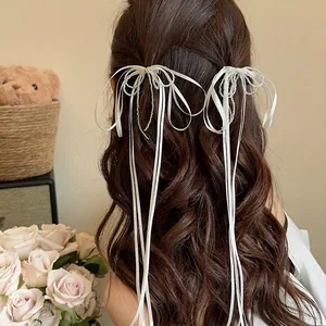 Elegant white bow hair clips with long ribbons and beads shown on a model's hair