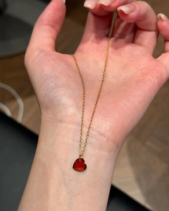 Handheld macro view of a red heart crystal pendant with a sleek gold-plated chain necklace