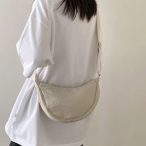 Close-up of beige nylon crescent bag with adjustable strap worn on a white t-shirt