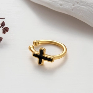 Close-up of golden ear cuff featuring a black cross design on textured background