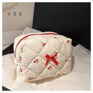 Detail shot of beige quilted makeup bag with red cherry pattern and a red bow accent