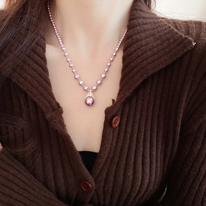 Gros plan d'un collier de perles mauves avec pendentif doré diamanté sur modèle