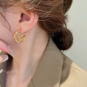 Macro side view of golden hollow C-shaped earrings with F-letter logo design on model