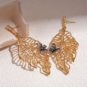 Artistic gold leaf earrings with silver butterfly accent on a minimalist background