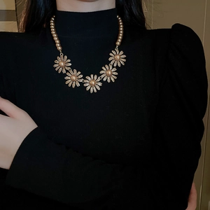 Detail of vintage gold flower necklace with pearls worn on a black turtleneck
