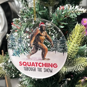 Acrylic Christmas ornament featuring Bigfoot in snow with festive SQUATCHING text