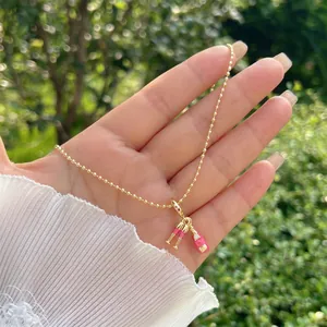 Dettaglio della collana a sfere dorate con ciondoli a bottiglia e calice in smalto rosa