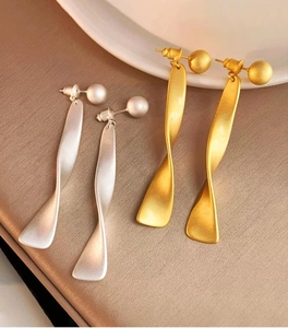 Macro shot of twisted matte metal pendant earrings in gold and silver finish