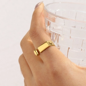 Detail of 18K gold-plated C-shaped ring on hand holding a textured glass cup