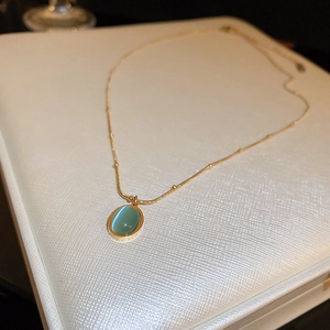 Macro shot of oval green cat eye stone pendant on a delicate gold bead chain necklace