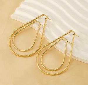 Detailed close-up of golden teardrop hoop earrings with polished finish on a minimalist board