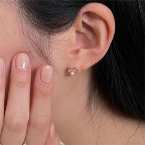 Close-up of heart-shaped gold pearl stud earrings worn on the earlobe for women