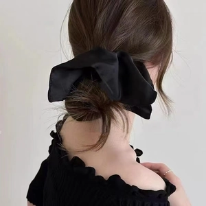 Glossy black satin oversized scrunchie bow hair tie styled on a person’s ponytail