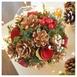 Close-up of luxury Christmas table decor with gold pinecones and red roses on white surface