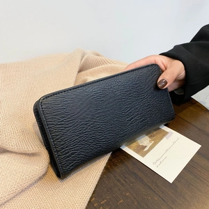 Schwarze lange Geldbörse mit Lychee-Ledertextur auf beigem Strickhintergrund