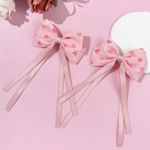 Detail of pink bow hair clips with red heart patterns and long flowing ribbons