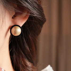 Close-up of retro black velvet and gold pearl stud earrings worn on a model's ear
