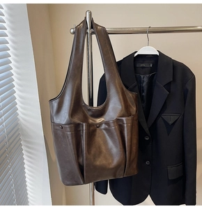 Detail of a large dark brown leather tote bag hanging next to a black blazer jacket