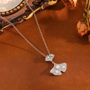 Macro view of silver ginkgo leaf pendant with pearls and crystals on textured background