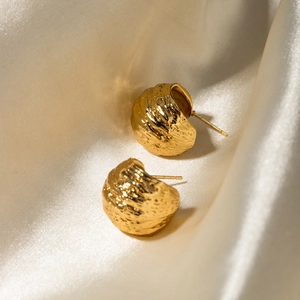 Detailed close-up of C-shaped 18k gold earrings with textured surface on beige silk