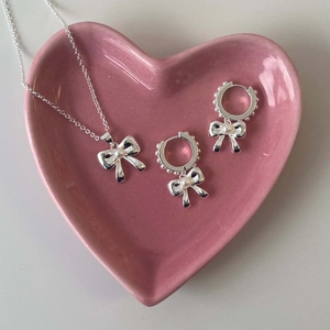 Detail view of silver bow necklace and earrings set with pearls on a pink heart plate