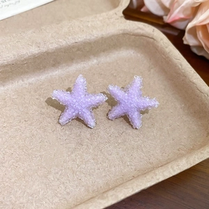 Gros plan de boucles d'oreilles étoile de mer mauves sur un plateau beige