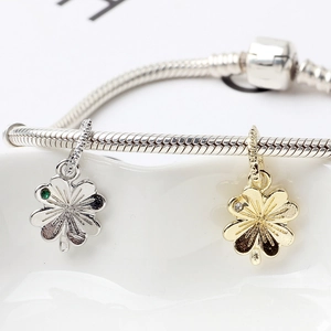 Close-up of gold and silver clover charms with inlaid gems on a snake chain bracelet