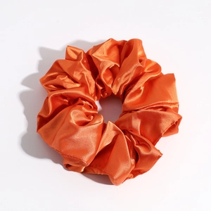 Detail view of glossy orange satin scrunchie showing smooth fabric texture and elastic design