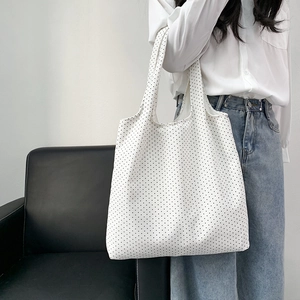 Detail view of a white floral tote bag with black dots worn over the shoulder by a model