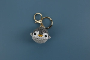 Detailed view of handmade crochet penguin keychain with golden metal clasp on blue-grey background