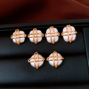 Macro view of gold-plated square cross earrings with white pearl beads on black tray