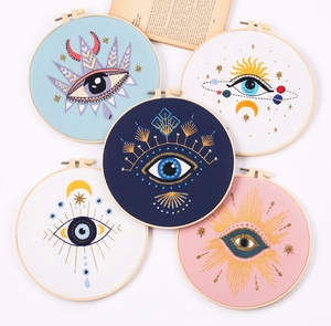Close-up of five finished eye-themed embroidery kits with wooden hoops on a vintage book