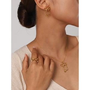 Golden stainless steel bow jewelry set featuring necklace earrings and ring on model