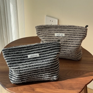 Detail of tweed makeup bags in black and beige with simple wish labels on a wood table