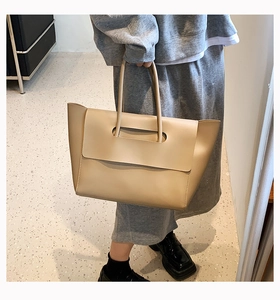 Detail of a large beige leather tote bag featuring a modern minimalist flap cover design