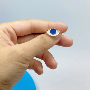 Close-up of a gold-plated evil eye ring with blue enamel detail held by a person