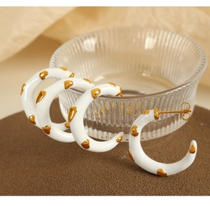 Macro detail of C-shaped white enamel earring with gold heart patterns and gold plating