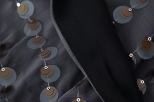 Detail of dark grey mesh fabric featuring multi-layered sequins and black trim craftsmanship