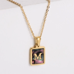 Close-up of a 18k gold rectangular pendant featuring letter M on iridescent shell inlay