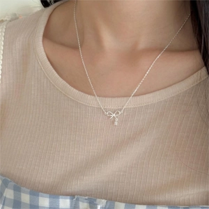 Close-up of a silver bow pendant necklace with zircon on a model's neck for a minimalist look