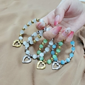 Stack of shiny cat eye beaded bracelets with heart charms held against beige fabric