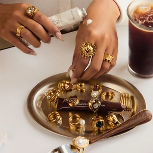 Detailed close-up of thick gold-plated rings with pearls and green gemstones on a tray