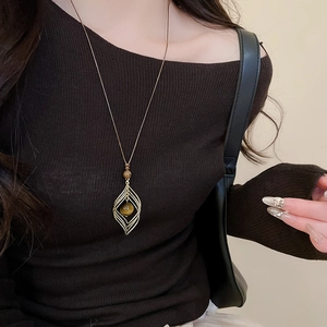 Detail of tiger eye rhombus pendant with golden hollow leaf frame on a simple cord