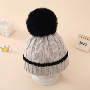 Detail of grey baby knit hat with large black faux fur pompom and cable knit texture