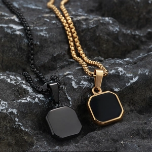 Detail of square black enamel pendants on box chains over dark natural stone background